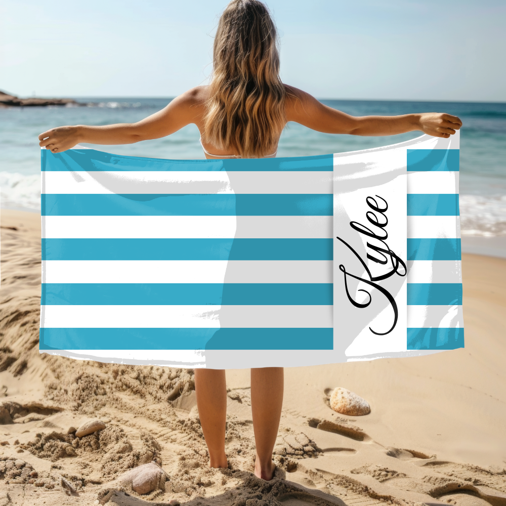 Person holding a blue and white striped towel with 'Kylee' on it at the beach.