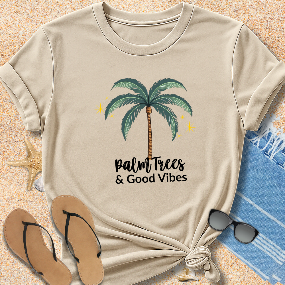 Beige t-shirt with palm tree design and 'Palm Trees & Good Vibes' text on sand with flip-flops and sunglasses.