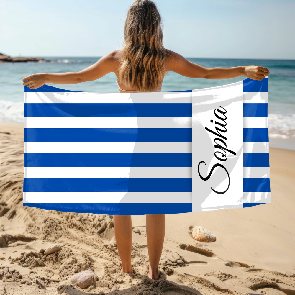 Person holding a blue and white striped towel with 'Sophia' on it at the beach.