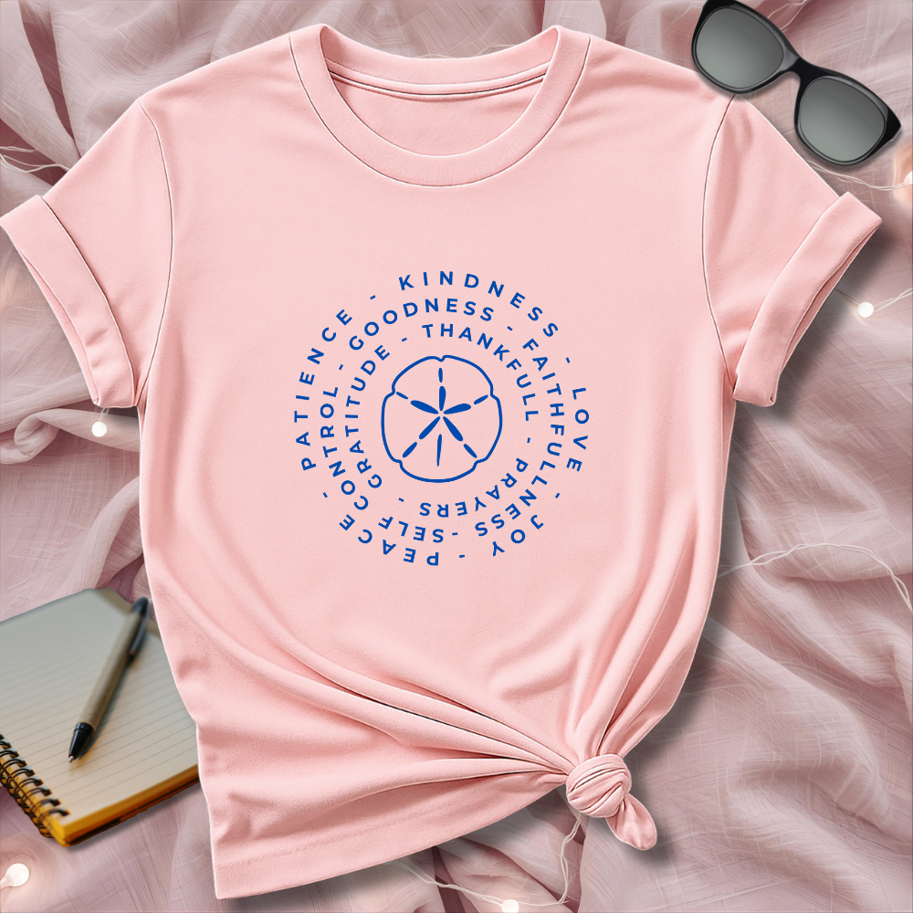 Pink t-shirt with motivational text design on a pink surface with sunglasses and notebook.