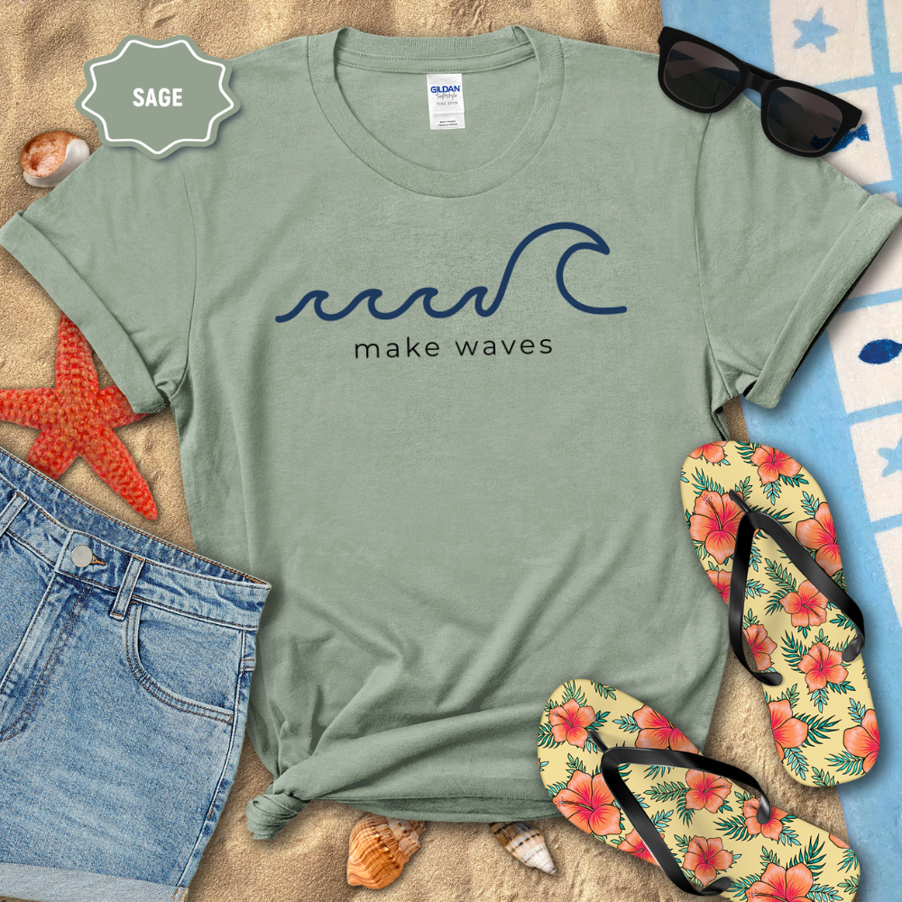 Sage green t-shirt with 'make waves' design on a beach setting with sunglasses, flip-flops, and starfish.