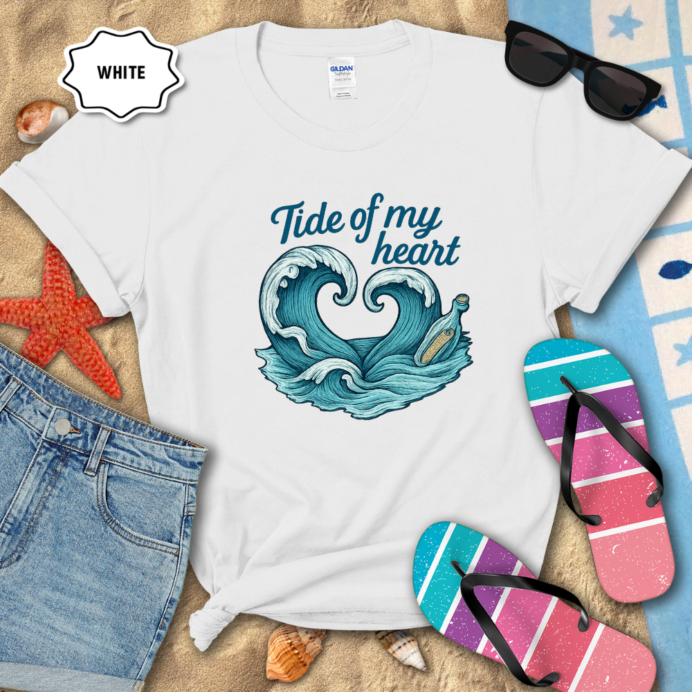 White t-shirt with ocean-themed design and beach accessories on sand