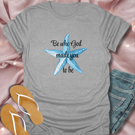Gray t-shirt with blue starfish and text on a pink surface with flip-flops and jeans.