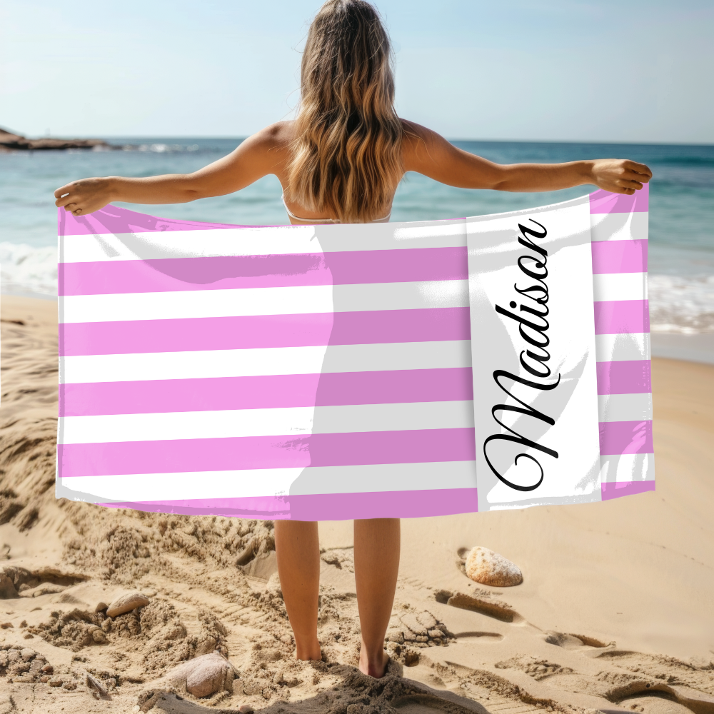 Person holding a pink and white striped towel with 'Madison' on it at the beach.