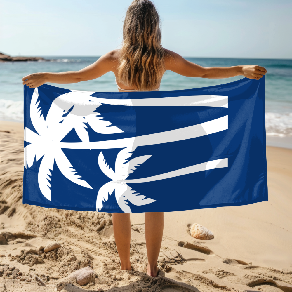 Person holding a blue towel with white palm tree design on a beach
