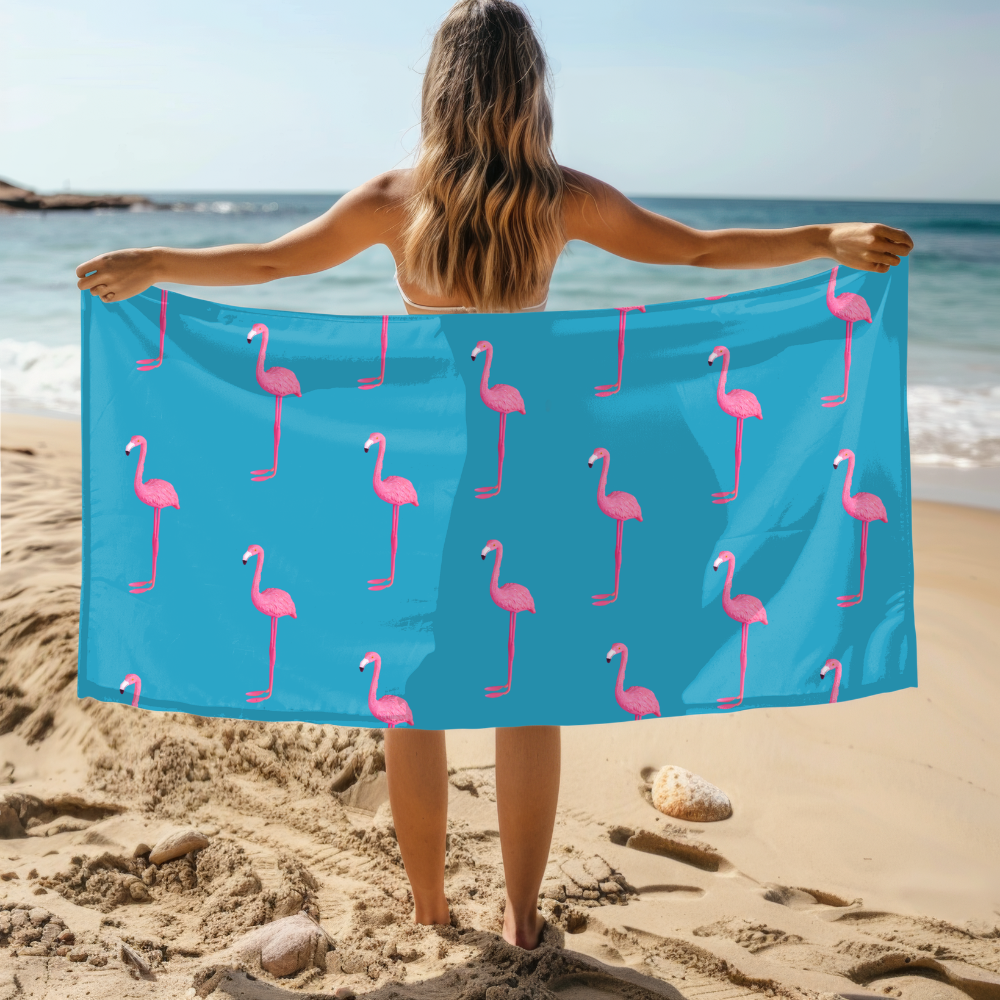Person holding a blue towel with pink flamingo pattern on a beach