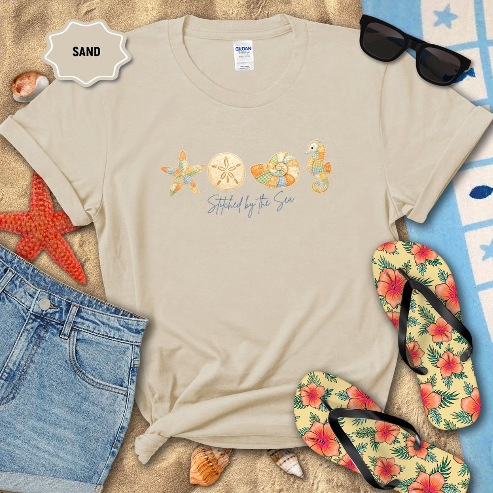 Beige t-shirt with beach-themed design on sand with flip-flops and sunglasses.