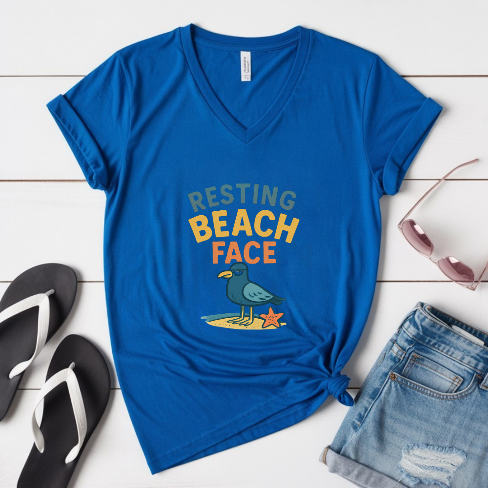 Blue t-shirt with 'Resting Beach Face' design on a wooden surface with flip-flops and shorts.