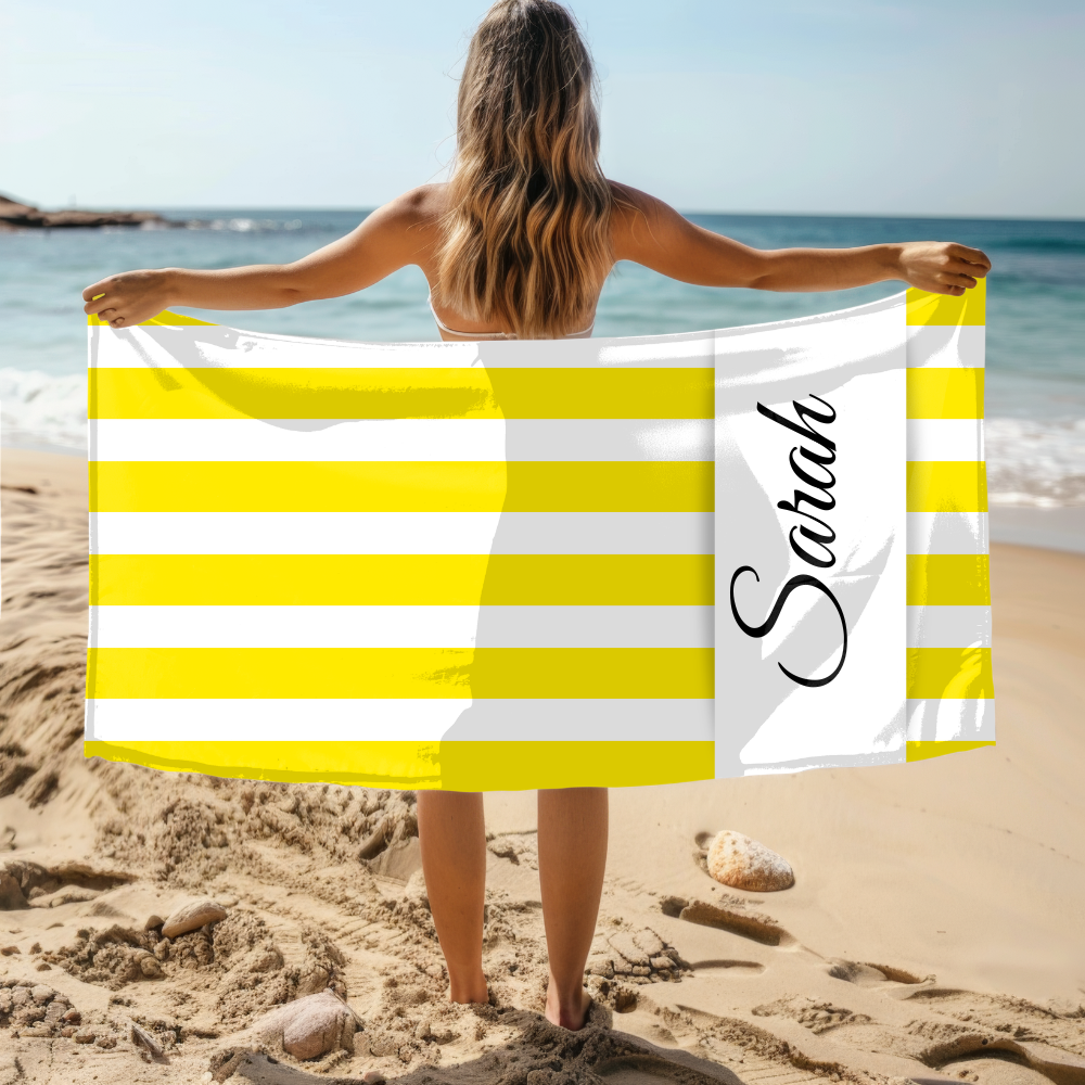 Woman holding a yellow and white striped towel with 'Sarah' on it at the beach.
