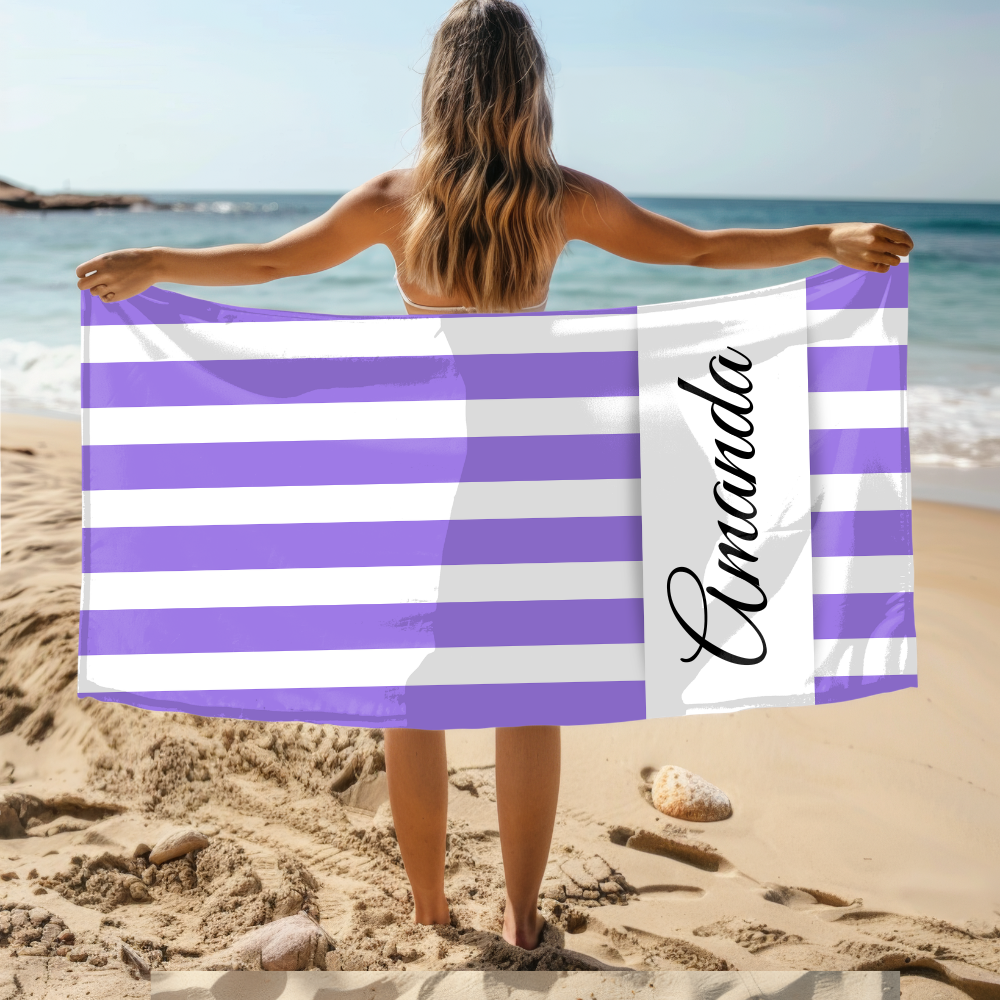 Person holding a purple and white striped towel with 'Amanda' on it at the beach.