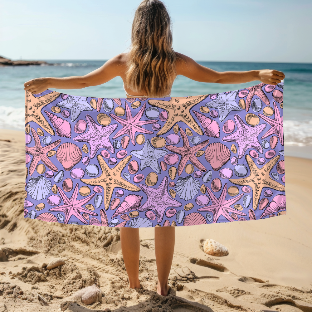 Person holding a beach towel with starfish and shell pattern on a sandy beach.