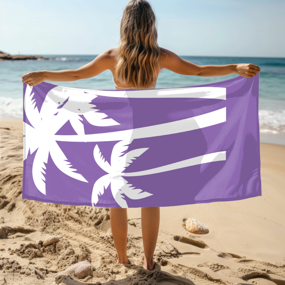 Person holding a purple beach towel with white palm tree designs on a sandy beach.
