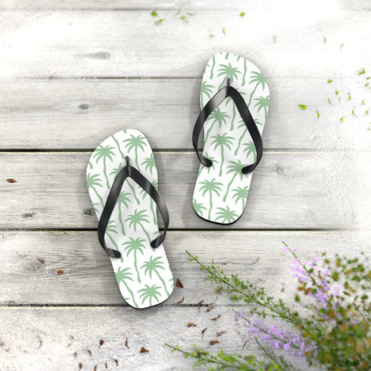 Pair of flip-flops with palm tree pattern on a wooden surface with flowers.