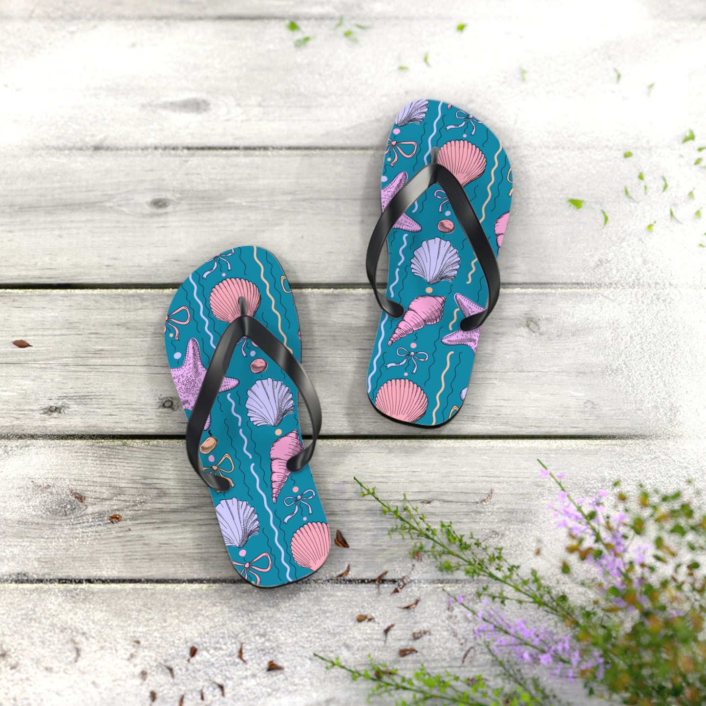Pair of blue flip-flops with pink shell design on a wooden surface with flowers.