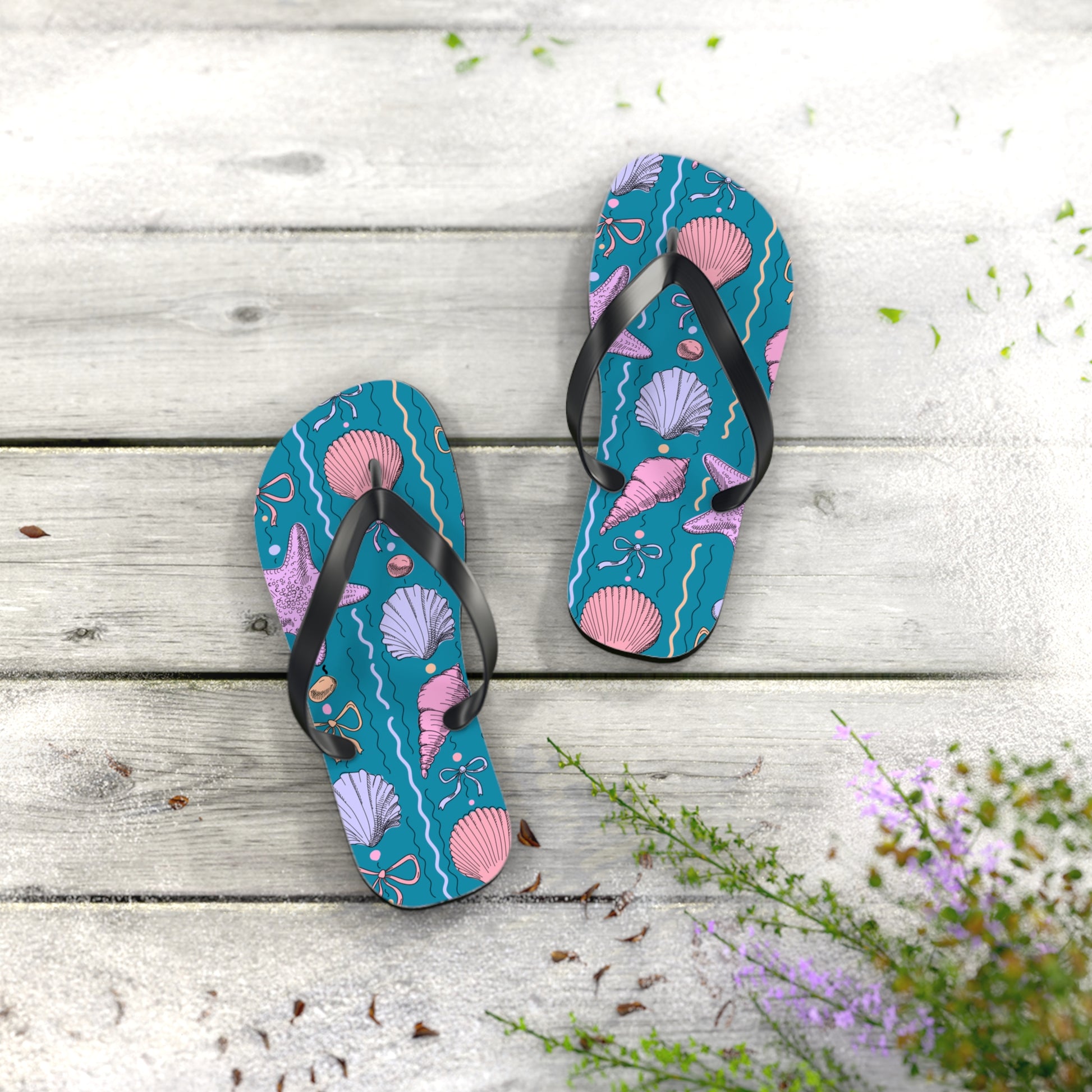Pair of blue flip-flops with pink shell design on a wooden surface with flowers.