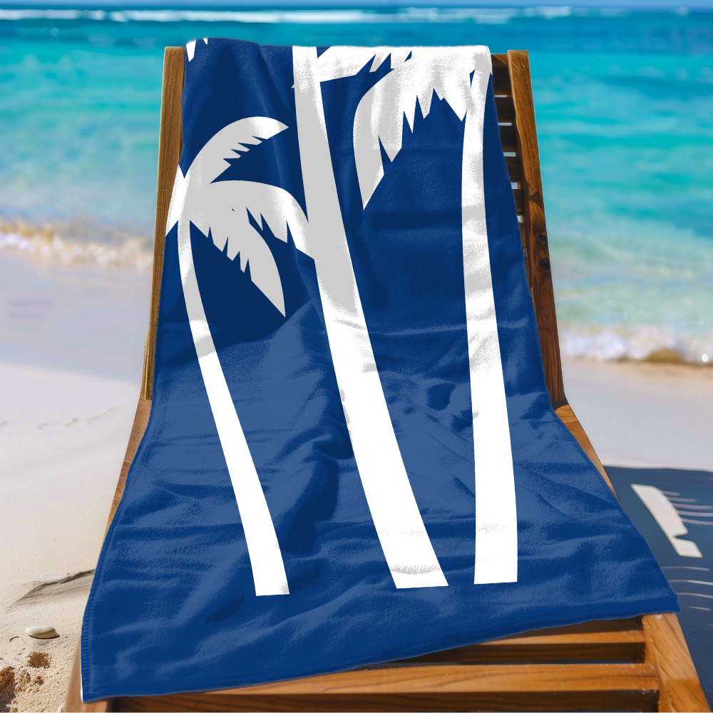 Blue beach towel with white palm tree design on a wooden chair at the beach.