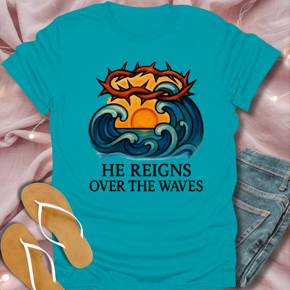 Turquoise t-shirt with a graphic design and text 'He Reigns Over The Waves' on a pink fabric background.
