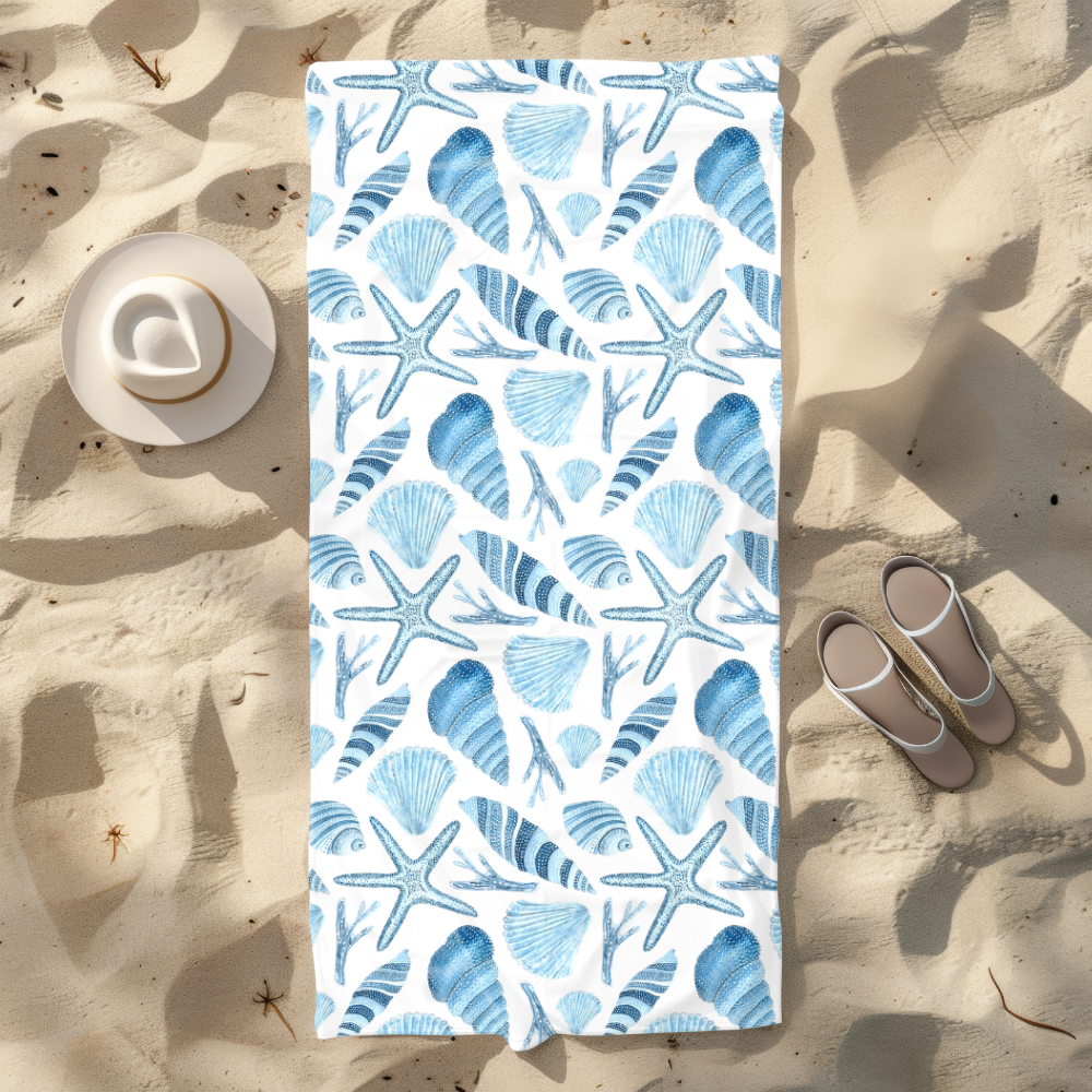 Beach towel with blue sea shell pattern on sand with hat and sandals