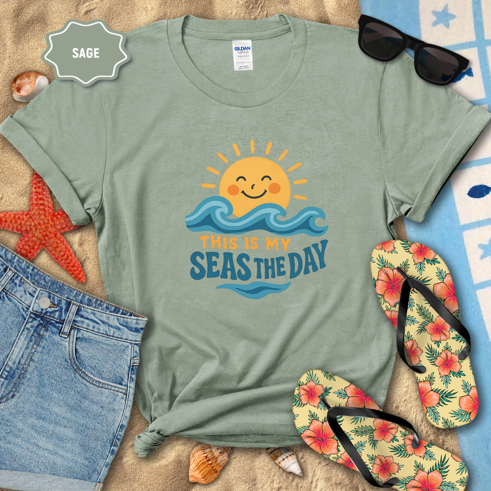 Sage green t-shirt with beach-themed design on a sandy background with sunglasses, flip-flops, and starfish.