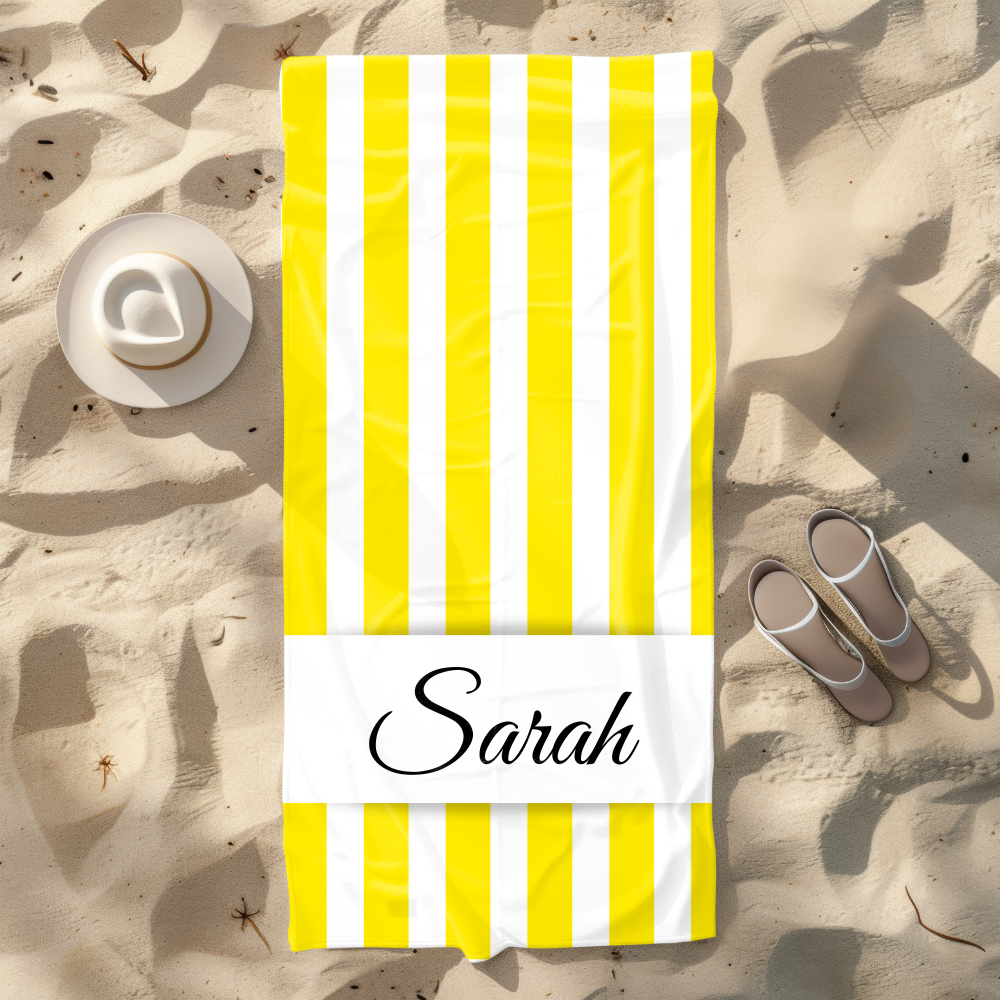 Yellow and white striped beach towel with 'Sarah' on a sandy background