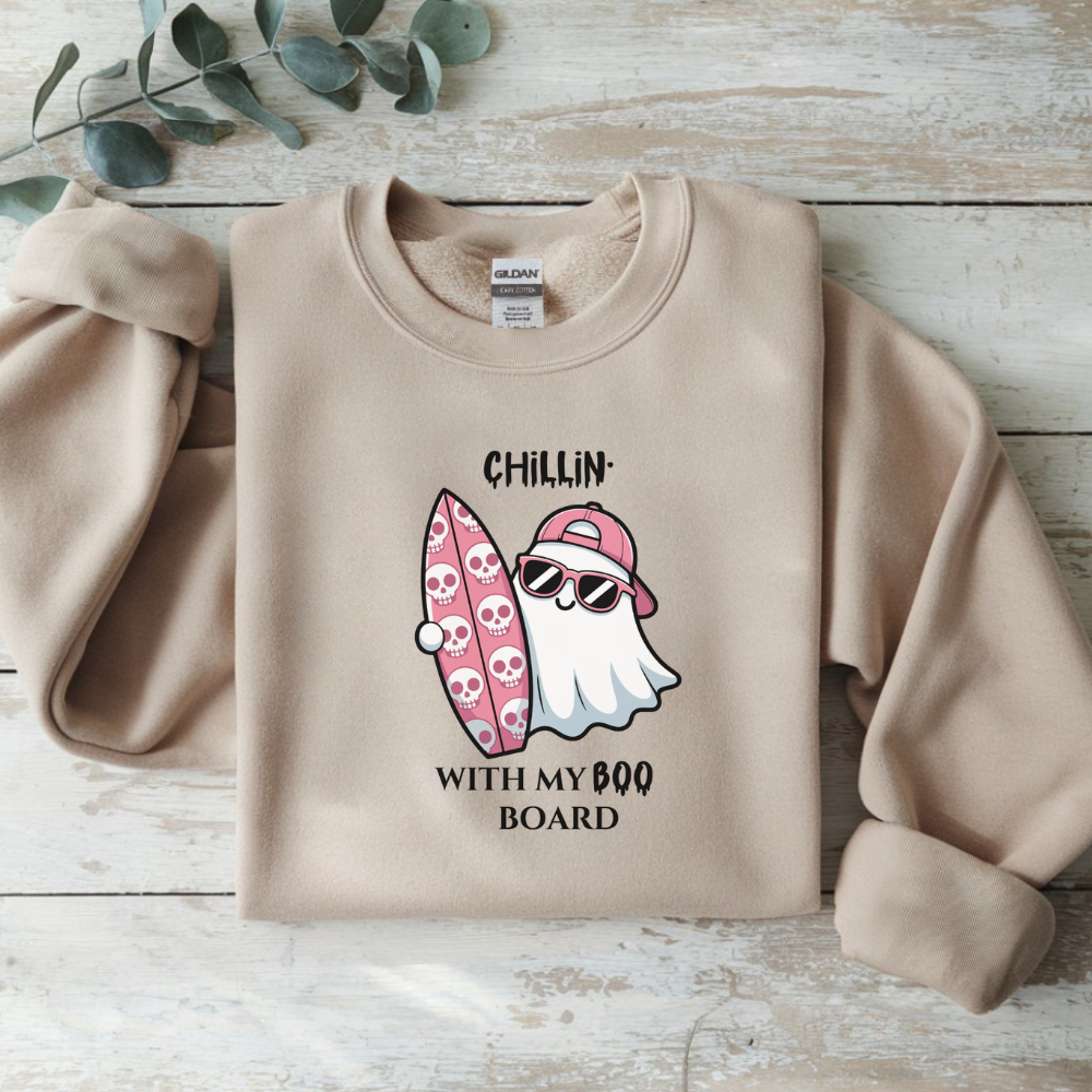 Beige sweatshirt with a ghost and surfboard graphic on a wooden surface