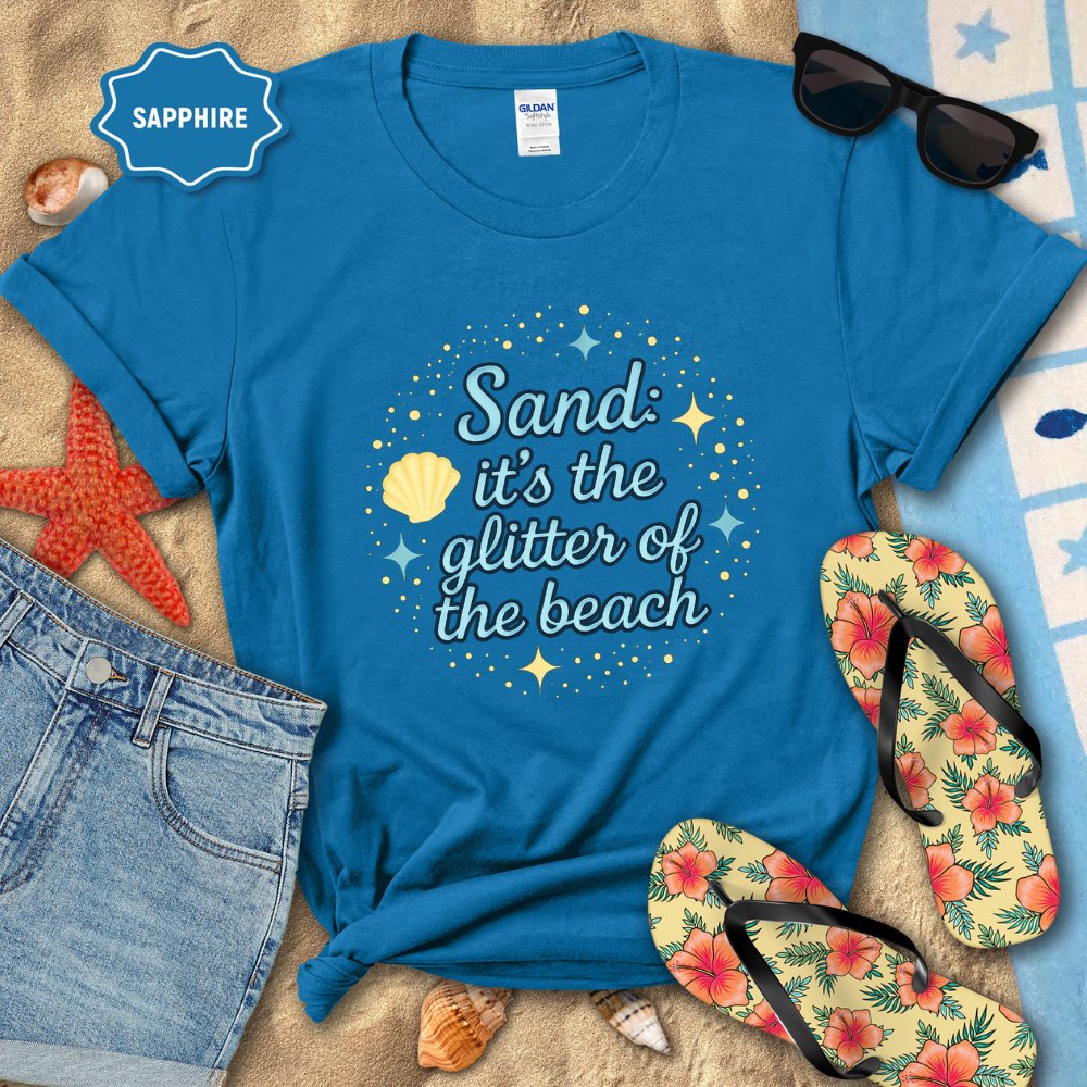 Blue t-shirt with beach-themed text, sunglasses, flip-flops, and sand toys on a sandy background.