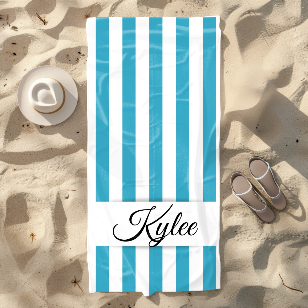 Blue and white striped towel with 'Kylee' on a sandy beach