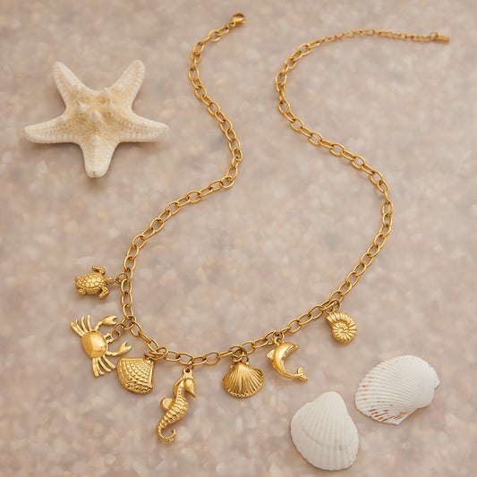 Gold necklace with charms on a sandy background with shells and a starfish.