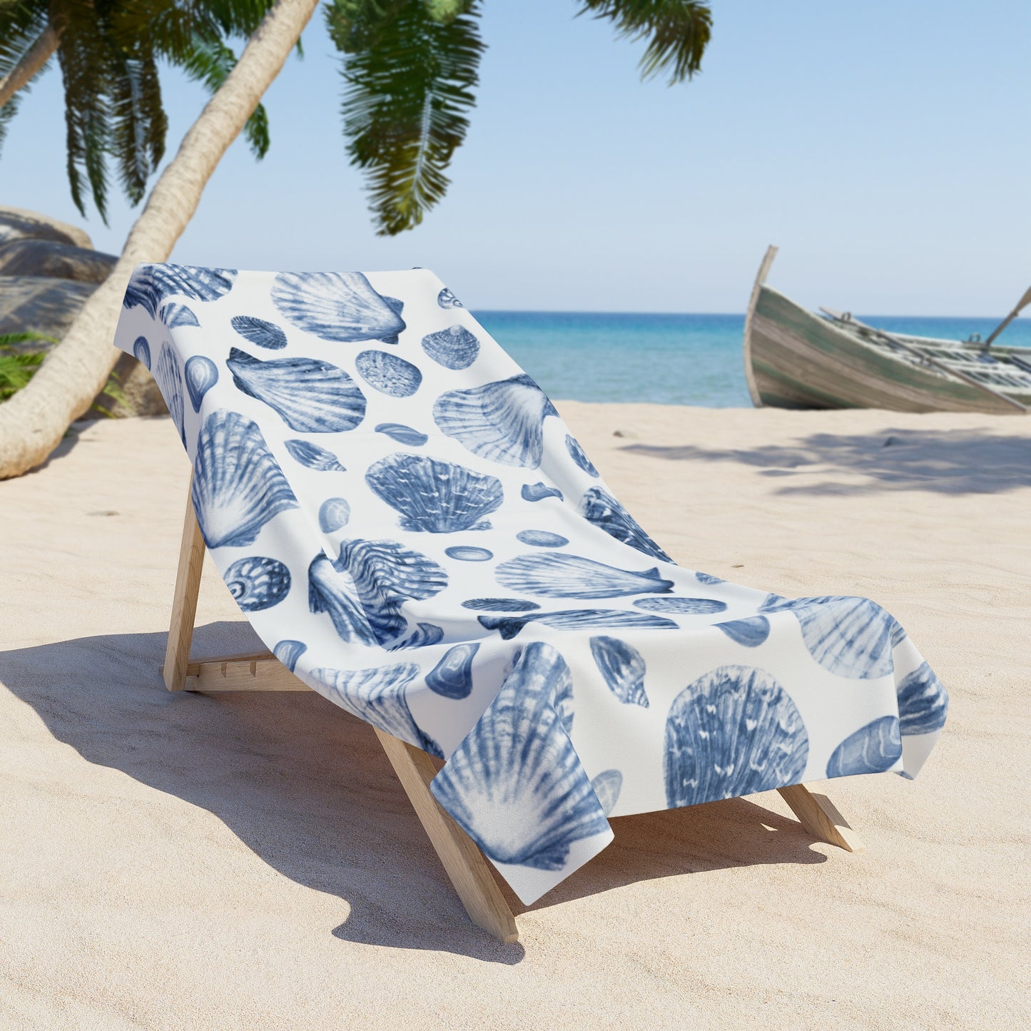 Beach chair with a blue shell patterned towel on a sandy beach with palm trees and a boat in the background.