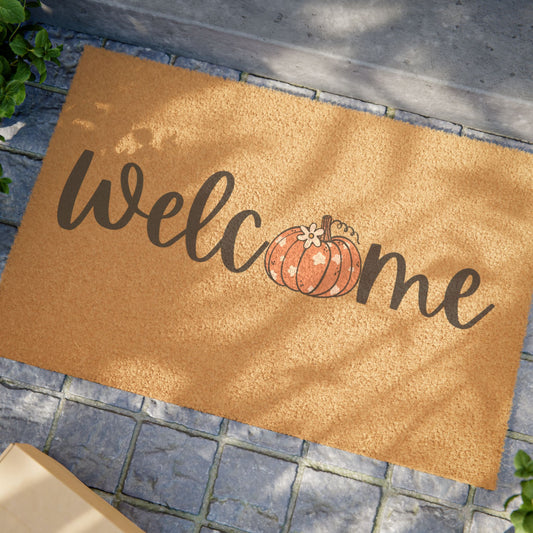 Doormat with 'Welcome' text and pumpkin design on a stone floor.