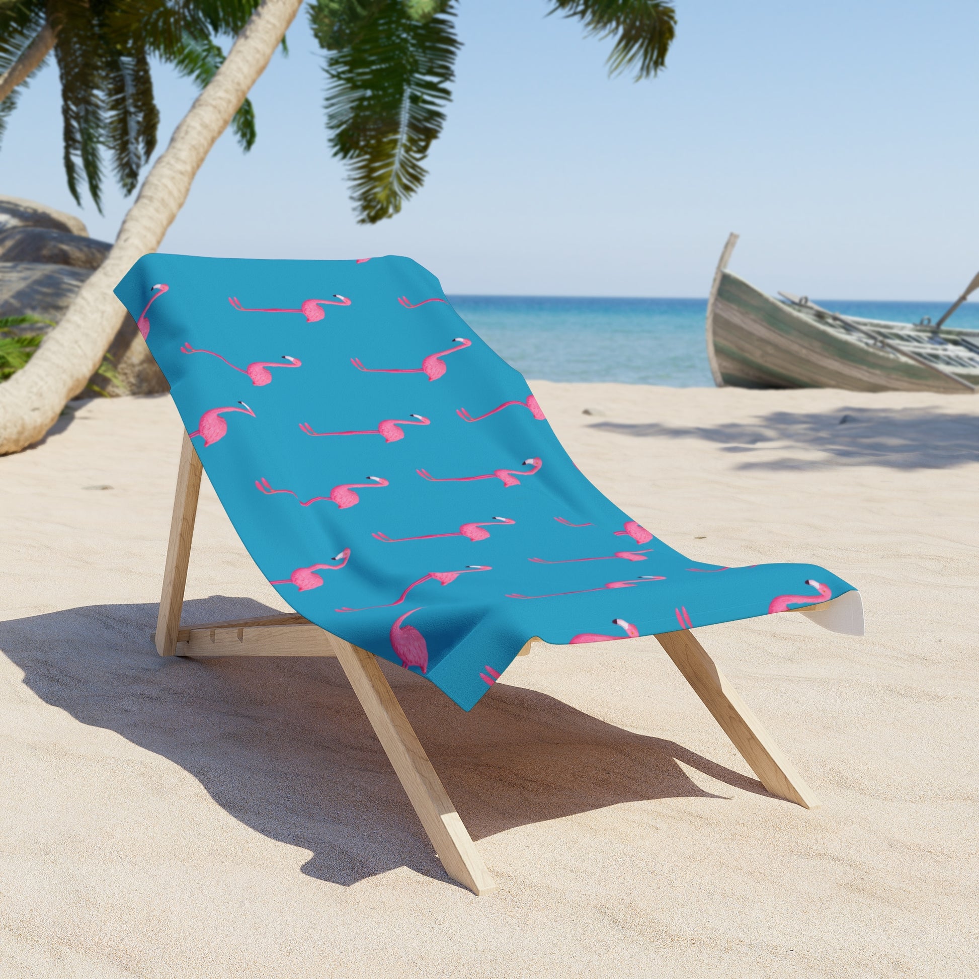 Blue beach towel with pink flamingo pattern on a wooden chair at the beach.