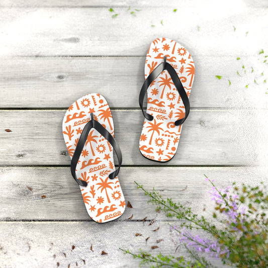 Pair of white flip-flops with orange floral patterns on a wooden surface with flowers.
