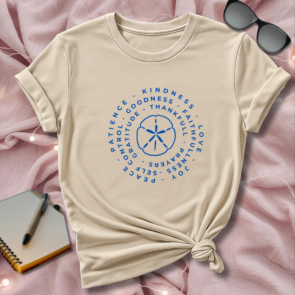 Beige t-shirt with blue circular design on a pink surface with sunglasses and notebook.