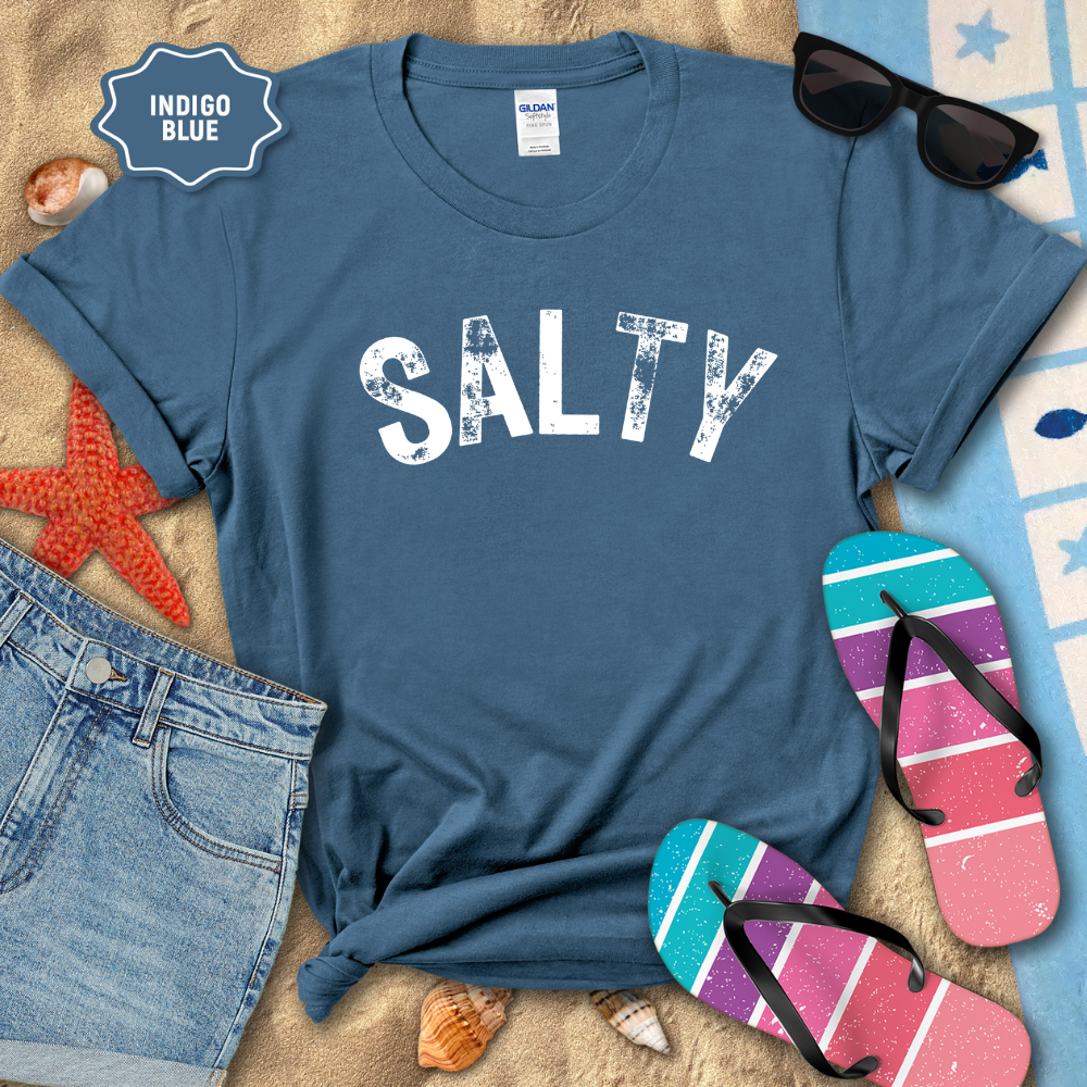 Indigo blue t-shirt with 'SALTY' text, sunglasses, and flip-flops on a beach setting.