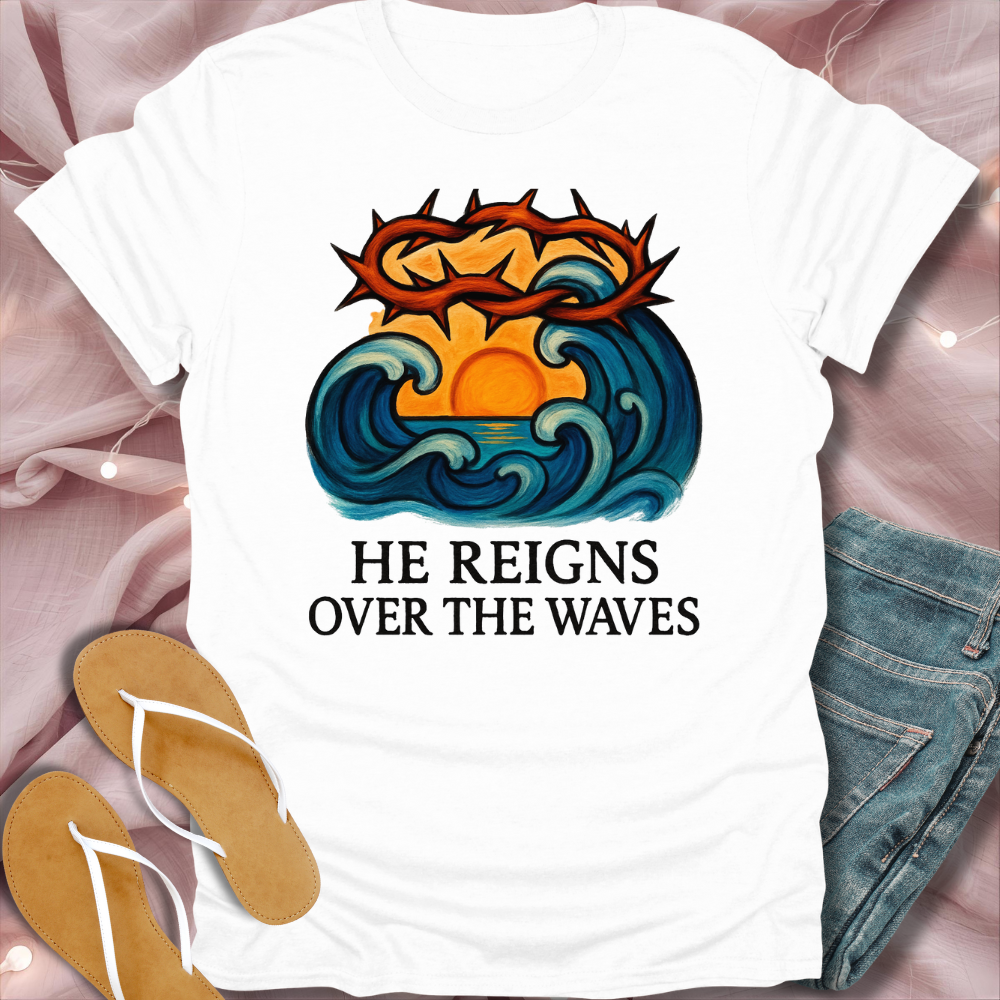 White t-shirt with a graphic design and text 'HE REIGNS OVER THE WAVES' on a pink fabric background.