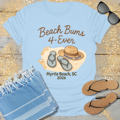 Light blue t-shirt with 'Beach Bums 4-Ever' design, sunglasses, towel, and flip-flops on a wooden surface.