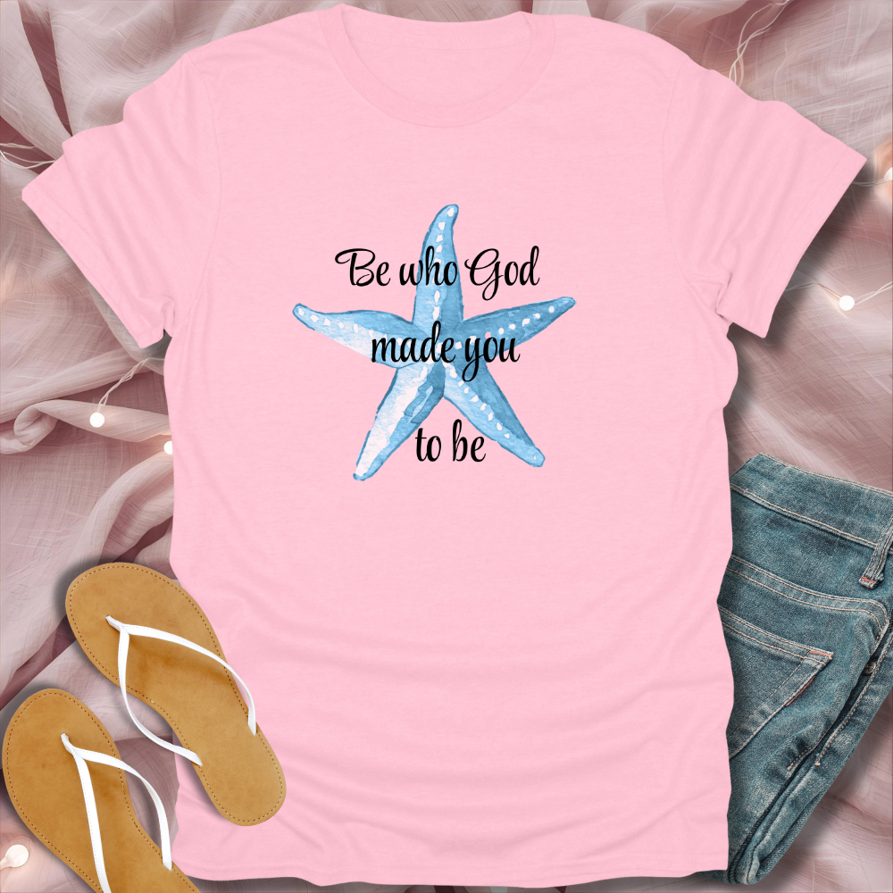 Pink t-shirt with a starfish design and text, placed on a soft pink surface with jeans and flip-flops.