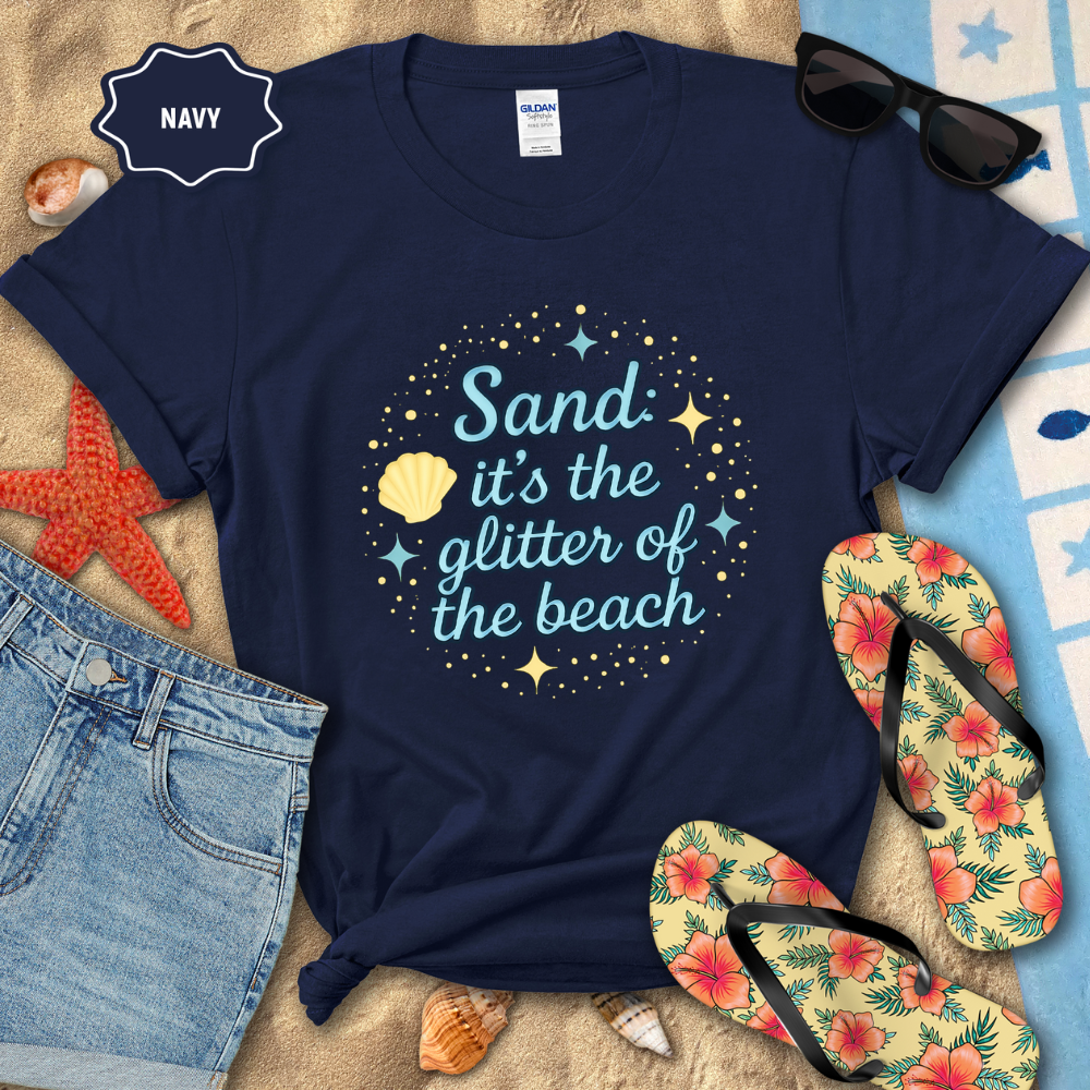 Navy t-shirt with beach-themed design on a sandy surface with flip-flops and sunglasses.