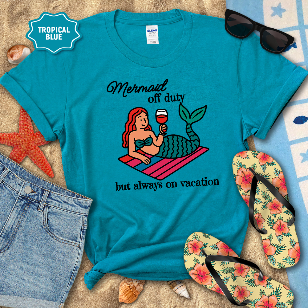 Blue t-shirt with mermaid graphic and text on a beach setting