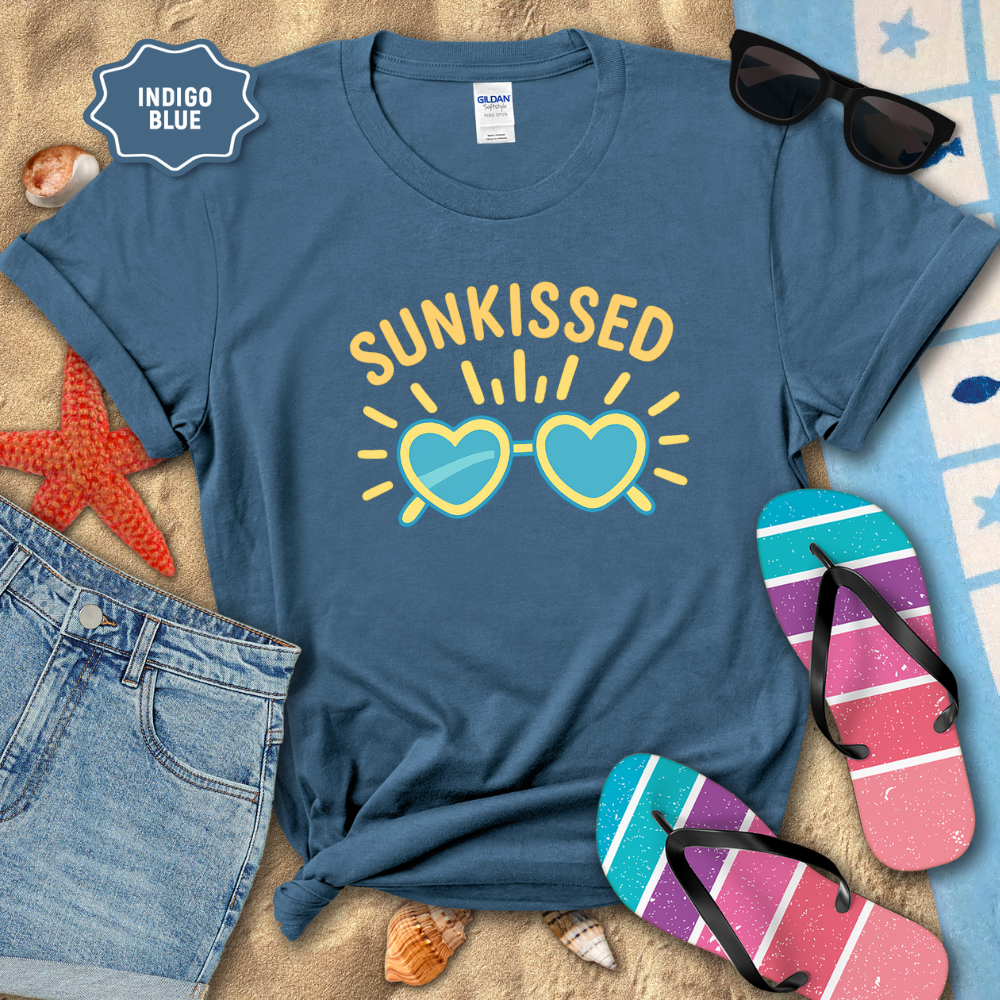 Blue t-shirt with 'Sunkissed' design on a beach setting with sunglasses, flip-flops, and denim shorts.