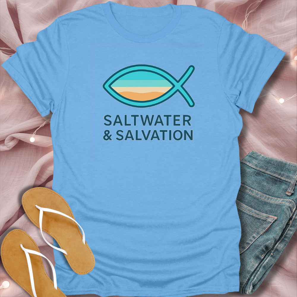 Blue t-shirt with 'Saltwater & Salvation' design on a pink surface with sandals and jeans.