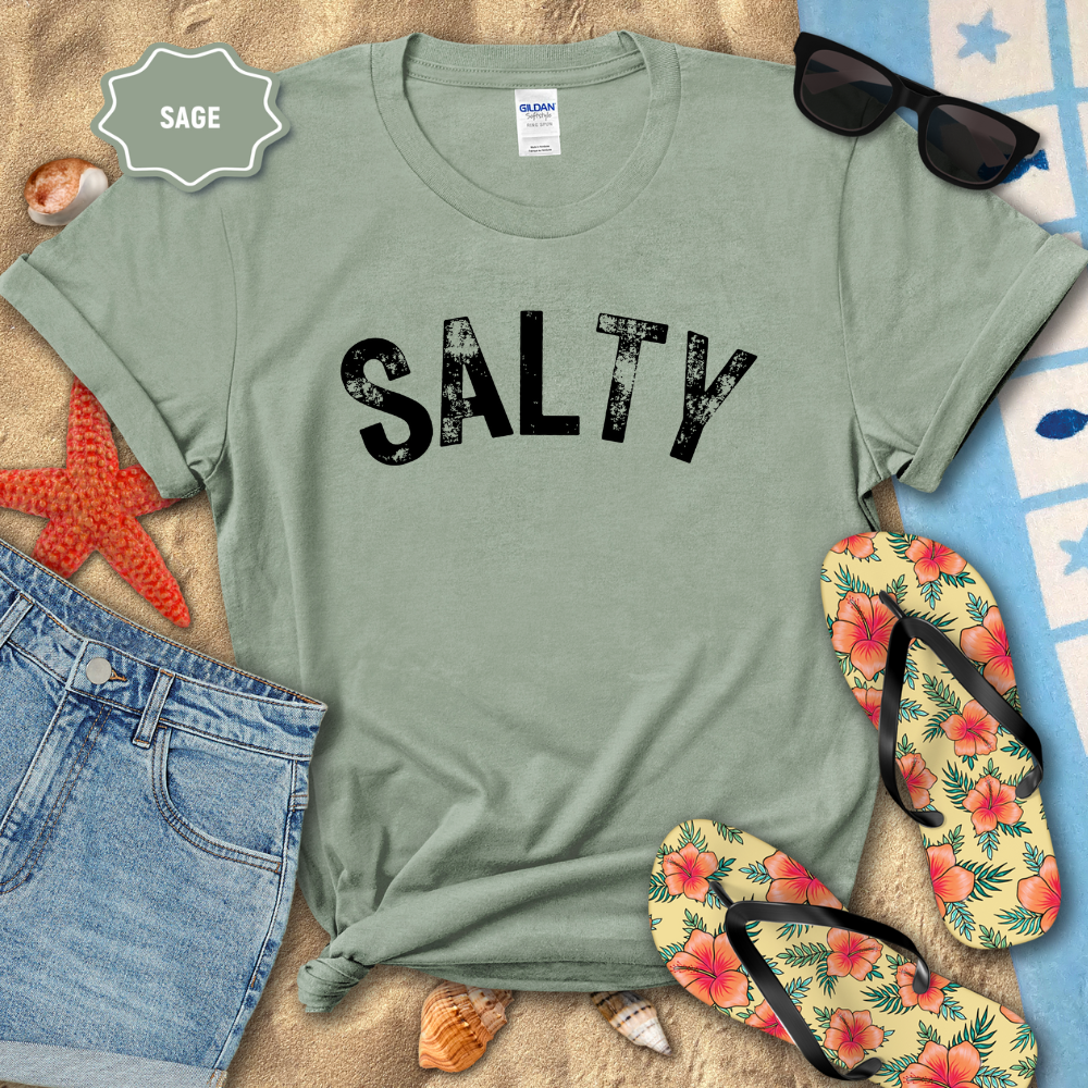 Sage green t-shirt with 'SALTY' text on a beach setting with sunglasses, flip-flops, and starfish.