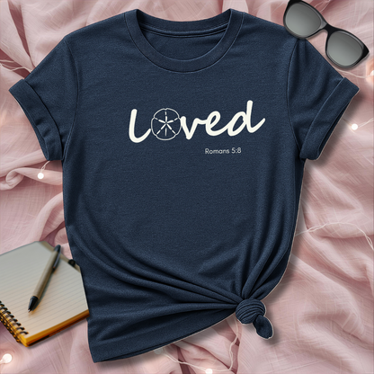 Navy blue t-shirt with 'Loved' text on a pink surface with sunglasses and notebook.