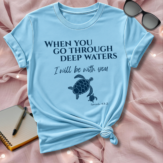 Light blue t-shirt with motivational quote and turtle graphic on a pink surface with sunglasses and notebook.