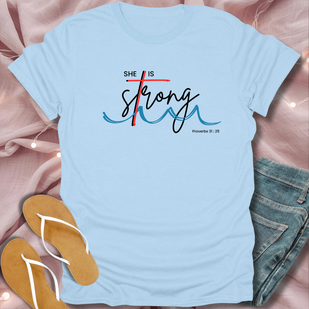 Light blue t-shirt with 'She is Strong' text on a pink fabric background