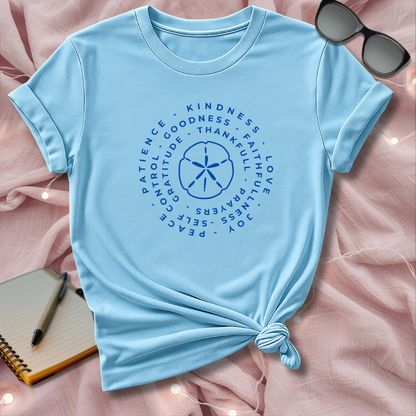 Light blue t-shirt with motivational text and design on a pink surface with sunglasses and notebook.