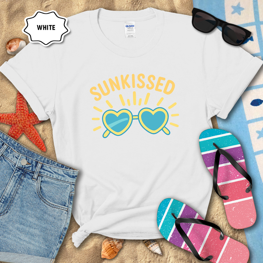 White t-shirt with 'Sunkissed' sunglasses graphic on a sandy background with beach accessories.