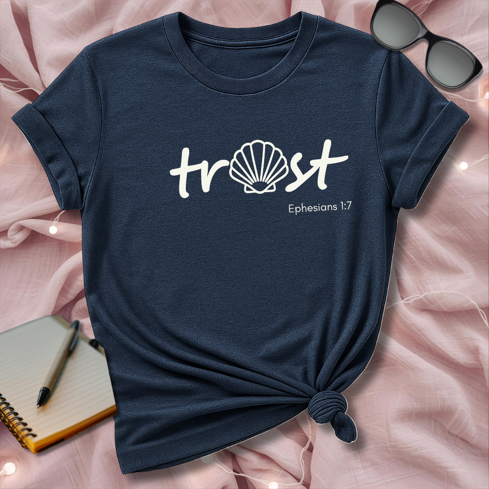 Navy blue t-shirt with 'trust' and 'Ephesians 1:7' text on a pink surface with sunglasses and notebook.