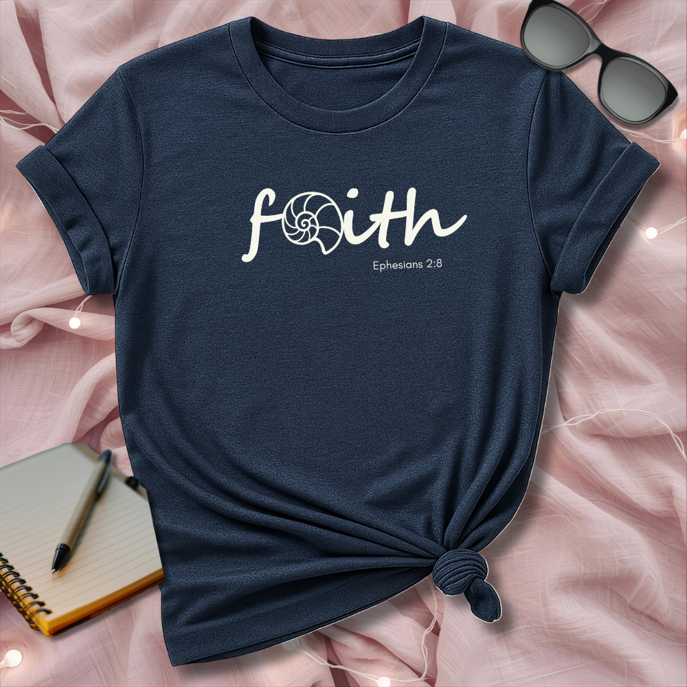 Navy blue t-shirt with 'faith' text on a pink surface with sunglasses and notebook.