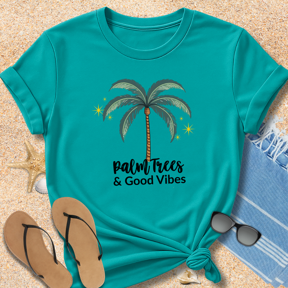 Teal t-shirt with palm tree design and 'Palm Trees & Good Vibes' text on sand with beach accessories.